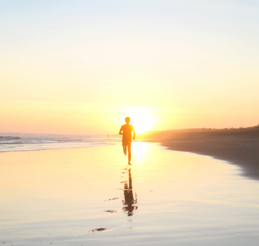 Man running on a beach shorefront into a dawn skyline